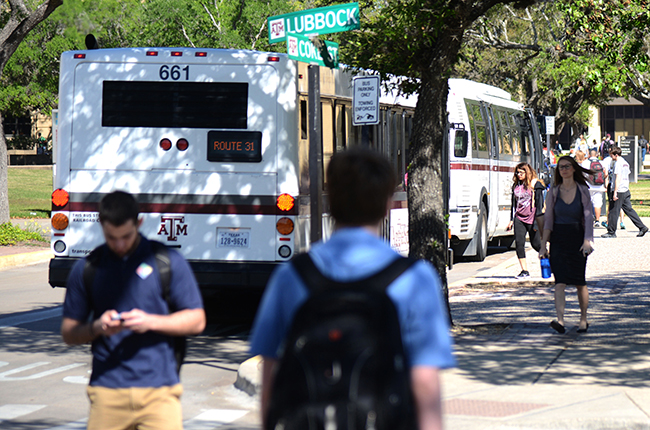 students walk past buss stopped on campus